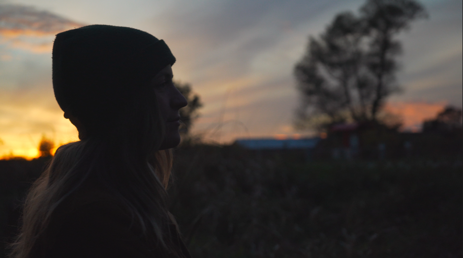Silhouette of a woman in a beanie gazing into a glowing sunset sky