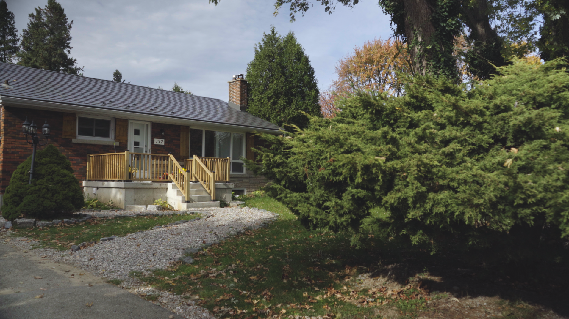 Front view of a red-brick bungalow surrounded by trees in autumn, with house number 172