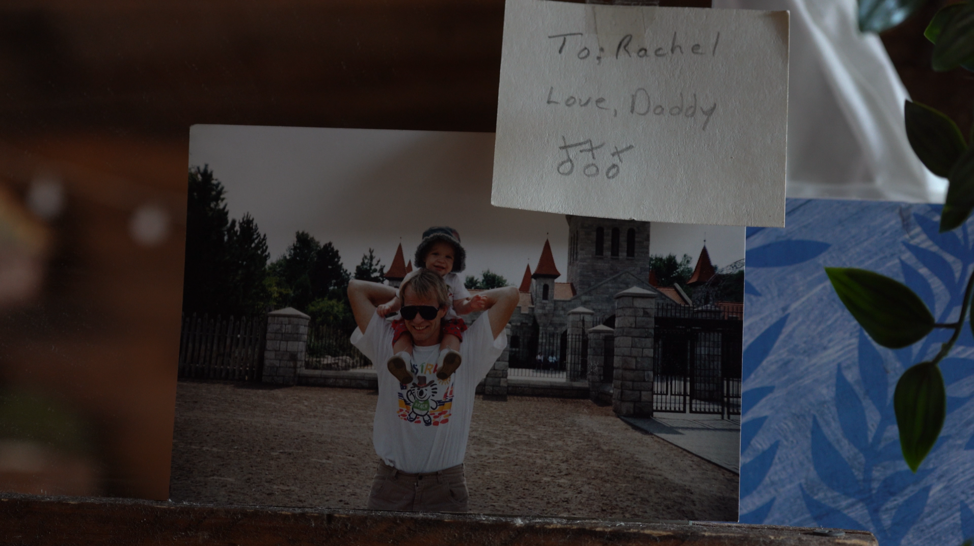 Old photo of a child on a man's shoulders at a theme park, with a handwritten note that says 'To: Rachel, Love, Daddy'