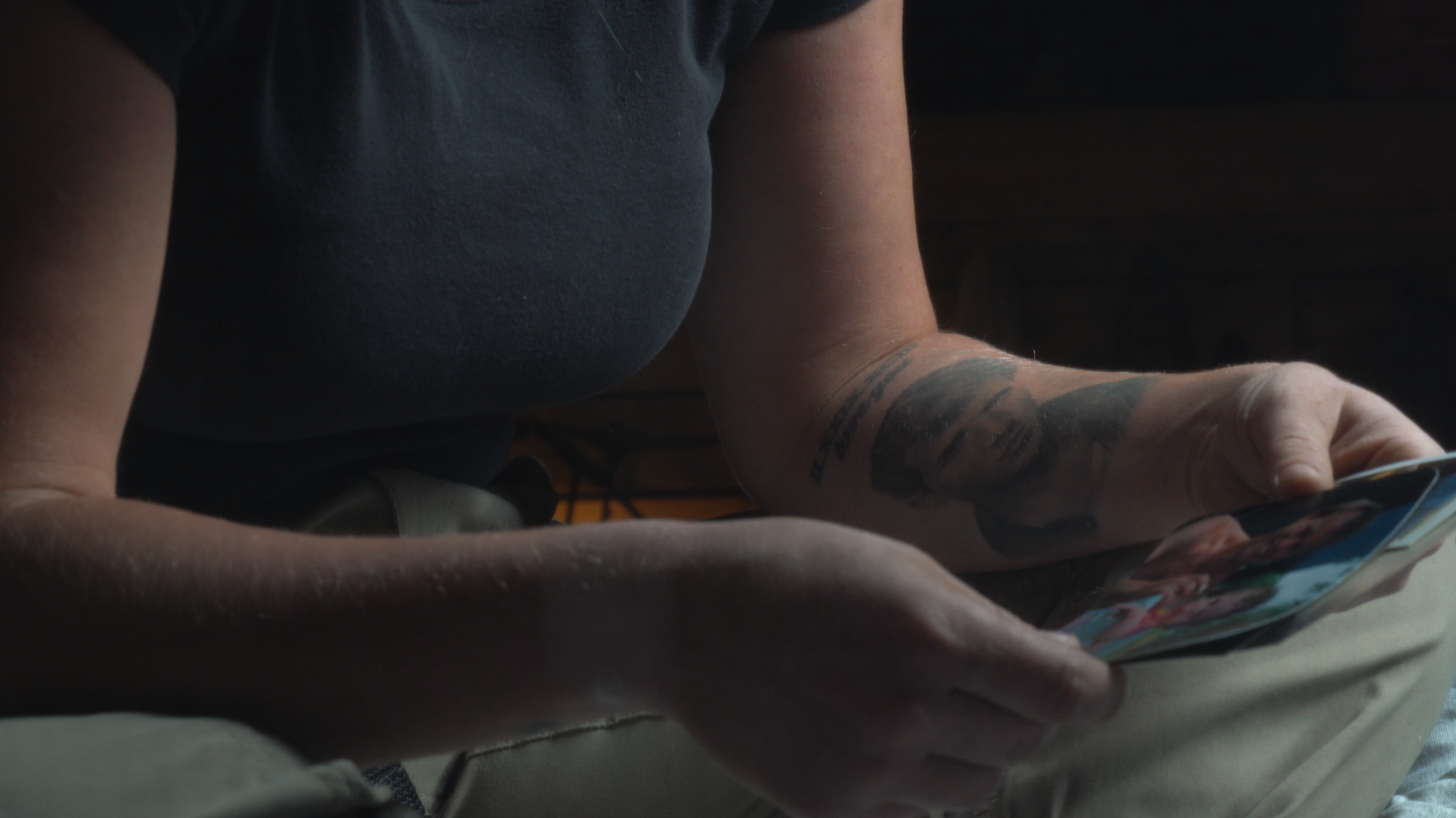 Close-up of a woman holding printed photos, with a tattoo of a man’s face on her arm